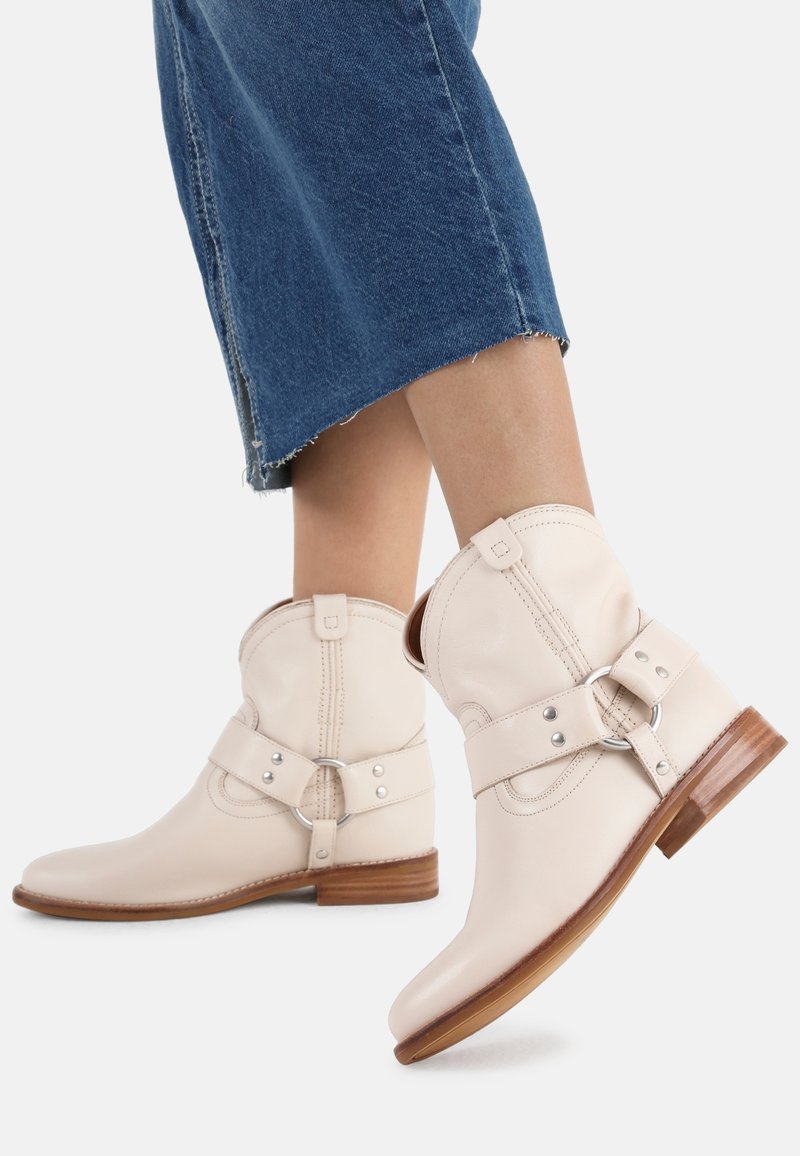 Bottines en cuir crème avec un bout rond, une sangle latérale dotée d'une boucle circulaire, et un petit talon en bois. Portées avec du denim.