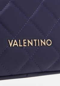 Navy prošívaná kožená peněženka s zlatým nápisem "VALENTINO", s diagonálním prošíváním vytvářejícím diamantový vzor a hladkou texturou.