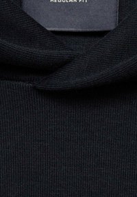 Czarny dzianinowy top o prążkowanej fakturze i złożonym kołnierzem. Metka informuje o "Regular Fit". Materiał wydaje się miękki i lekki.