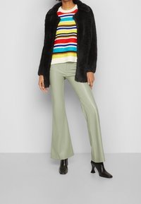 Musta tekoturkisviitta monivärisen raidallisen neuleen päällä, yhdistettynä vaaleanvihreisiin tekonahkahousuihin ja mustiin nappikorkokenkiin.