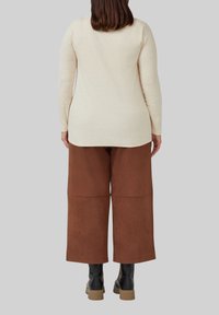 Beige lange mouw top met een relaxte pasvorm, gecombineerd met brede bruine broek. De outfit heeft een gladde textuur met een subtiele glans.