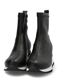 Botas de tobillo de cuero negro con tacón de cuña, que presentan una cremallera lateral, una suela blanca en contraste y una textura suave.