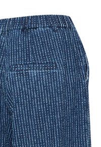 Pantalones de mezclilla azul con un patrón de costura blanca vertical, que cuentan con un bolsillo trasero de welt y presillas para el cinturón.