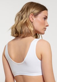 Bralette bianco in cotone con spalline larghe, design a schiena bassa e fascia elastica morbida. Texture liscia senza hardware visibile o motivi.