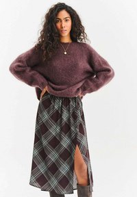 Sweter z moheru w kolorze winnej czerwieni o luźnym kroju i szerokich rękawach, zestawiony z plisowaną spódnicą w ciemnych odcieniach jagody i niebieskiego z bocznym rozcięciem.