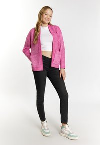 Ružový pletený kardigan s otvoreným predným dielom, dvoma prednými vreckami, nosený cez biely crop top a čierne džínsy, skombinovaný s multigeneračnými teniskami.