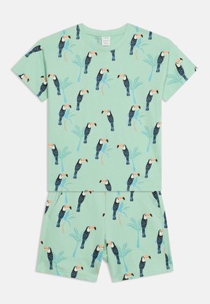 Lysegrønt sæt med kortærmet skjorte og shorts med spredte sorte og hvide tukaner og palmetræillustrationer.