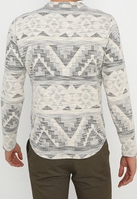 Camicia a maniche lunghe con un motivo geometrico in bianco e nero, realizzata in un tessuto a maglia testurizzato e con un orlo arrotondato sul retro.