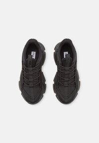 Chaussures de sport noires avec une tige en mesh texturé, un bout arrondi et une languette rembourrée. Elles disposent de lacets élastiques et d'une semelle coussinée pour le confort.