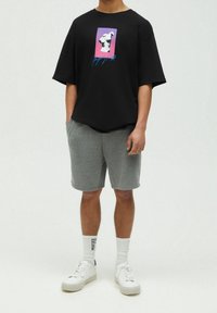 T-shirt noir oversize avec impression graphique représentant une sculpture sur un fond dégradé, associé à un short gris et des baskets blanches.