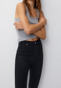 Top sin mangas de ribete gris combinado con jeans negros de tiro alto. El top tiene un escote cuadrado, mientras que los jeans tienen bolsillos delanteros y una textura suave.