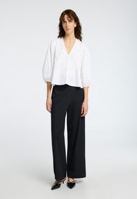 Blouse blanche à manches bouffantes, décolleté en V et motif brodé subtil, associée à un pantalon large noir taille haute.