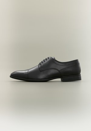 Chaussure habillée pour homme en cuir noir avec laçage fermé, bout droit et petit talon empilé, vue de profil sur fond neutre.