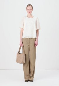 Kvinnors vit ögonlapp blus med korta ärmar, tillsammans med beiga höga byxor. Modellen håller en mjuk beige toteväska.