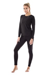 Långärmad svart träningströja och åtsittande svarta leggings i stretchtyg, accentuerade av minimal branding på bröstet och vid vristerna.