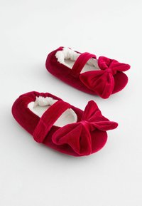Pantofole di velluto rosso con foderatura in pelliccia bianca, dotate di un ampio fiocco sulla parte anteriore e di una fascia sopra. Forma morbida e arrotondata.