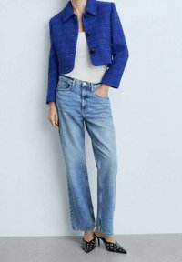 Giacca cropped in tweed blu con bottoni neri, abbinata a jeans con gamba dritta in lavaggio chiaro e scarpe col tacco nere a punta con dettagli in occhietto.