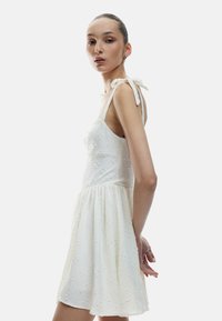 Vestido blanco con tela texturizada, forma A-line, tirantes ajustables, patrones florales y un cuerpo ajustado que fluye hacia una falda acampanada.