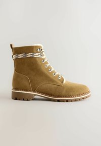 Tan mocka snörboot med shearling-fodring, slitstark sula och mönstrade snören för kallt väder.