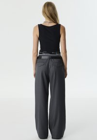 Zwarte mouwloze top gecombineerd met hoogopgetrokken grijze wijde broek met achterzakken en een contrasterende tailleband.