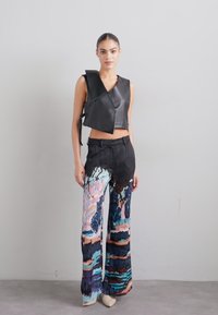 Svart skinnkort vest med vinkelaktig design; fargerike, abstrakte mønstrede vide bukser med blå, rosa og jordfarger.
