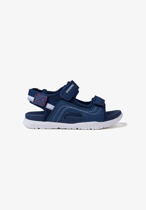 Sandalia infantil azul marino con suela blanca, correas ajustables de velcro, detalle de costuras rojas y correa con marca sobre fondo blanco.