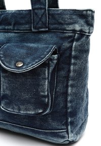 Denim-totepåse med en blekt blå finish, med en framficka med en silverfärgad tryckknapp och stabila handtag för bärande.