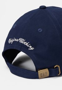 Marineblå bomulds-kasket med broderet "Original Clothing" tekst, justerbart bånd med metallspænde, som har "GAP" logo.