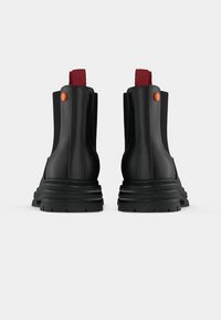 Botines negros hasta el tobillo con una textura suave, que cuentan con una lengüeta roja y un botón de acento naranja, además de una suela resistente para mayor tracción.