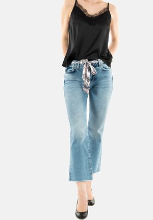 Camisola nera di raso con pizzo, jeans svasati blu chiaro, foulard a fantasia floreale legato in vita e scarpe con tacchi alti nere.