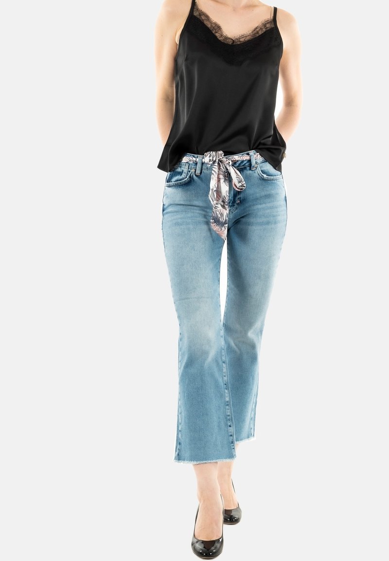 Camisola nera di raso con pizzo, jeans svasati blu chiaro, foulard a fantasia floreale legato in vita e scarpe con tacchi alti nere.