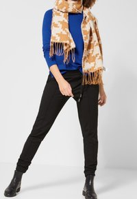 Blå långärmad topp, svarta smala byxor och en mönstrad brun scarf med fransar. Svarta ankle boots fulländar outfiten.