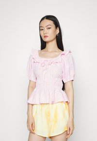 Blusa riscada em rosa e branco com decote com babados, mangas curtas abalonadas e cintura peplum, adornada com pequenos padrões de pontos amarelos.