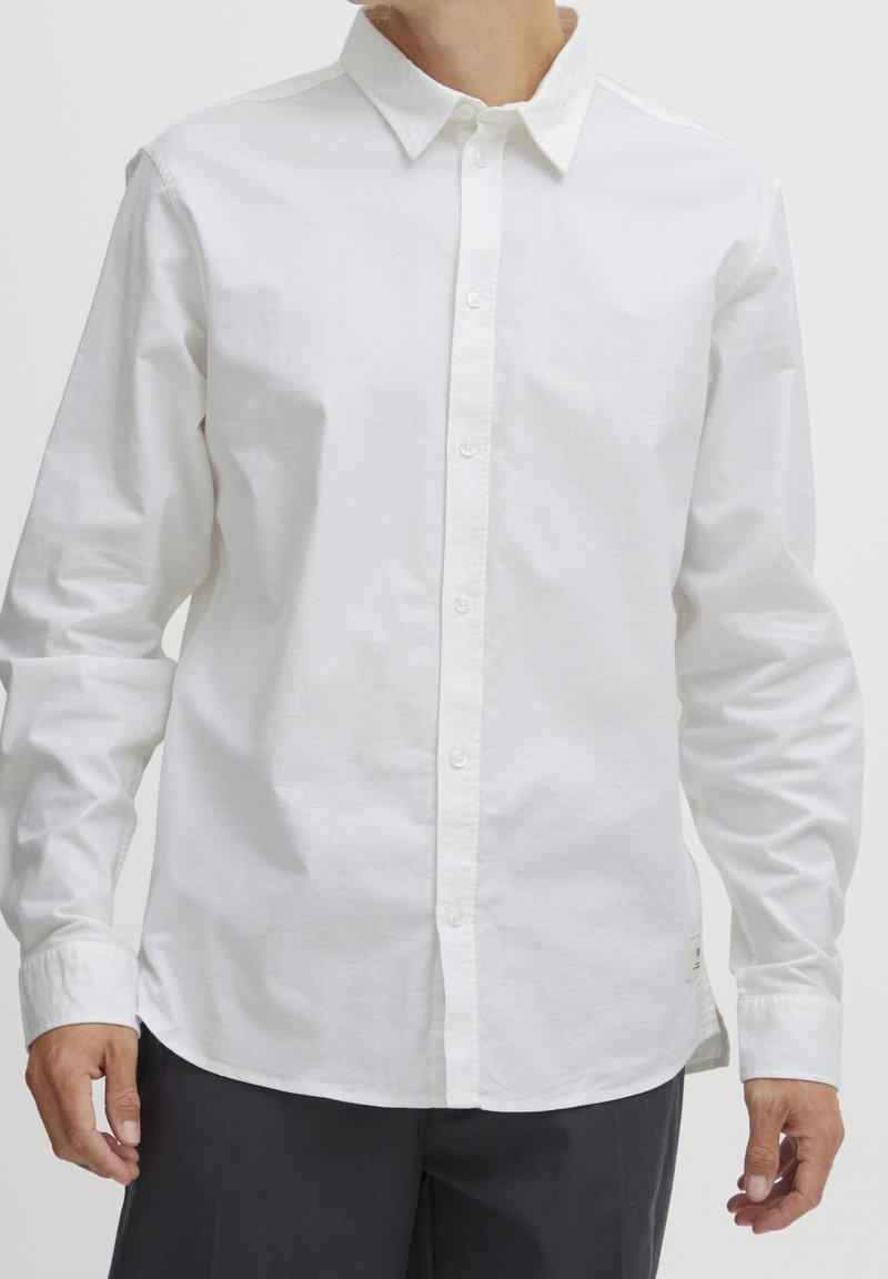 Camisa blanca de manga larga y botones hecha de algodón. Presenta un cuello clásico, tapeta frontal y una superficie texturizada sutil. Corte casual.