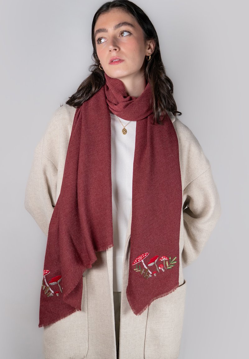 Écharpe bordeaux en tissu doux, ornée de champignons rouges brodés et de feuillage vert aux extrémités, avec des bords à franges discrètes.