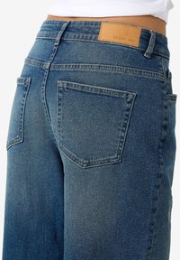 Vervaagde blauwe denim jeans met een rechte pijp, voorzien van twee achterzakken en een tan leren label aan de taille.