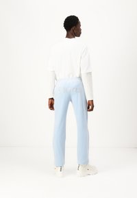 Pantaloni jogger azzurro chiaro con vita elasticizzata, caratterizzati dalla scritta "Pesci" in lettere argentate lucide sul retro, abbinati a una maglietta bianca a maniche lunghe.