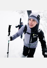 Water-resistant jacket in light purple and black, featuring a zippered front, pockets, and adjustable straps. Snow-covered background.