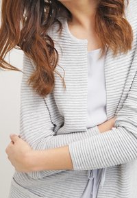 Cardigan grigio chiaro a coste con colletto a scialle, maniche lunghe e vestibilità rilassata. Strato interno di un grigio più chiaro visibile sotto.