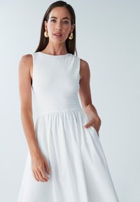 Balta be rankovių suknelė su tekstūruotu liemeniu, siaurėjančia juosmens dalimi ir plačia sijono dalimi. Su kišenėmis, pagaminta iš glotnios, lengvos medžiagos.