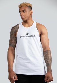 Fehér pamut ujjatlan póló, fekete logóval és "GORILLA WEAR" felirattal. A dizájn ujjatlan fazonú és laza illeszkedésű.