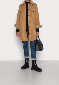 Brun ullblandad oversized skjortjacka med svarta knappar, två bröstfickor, kombinerad med blå jeans och svarta chunky ankelskor.