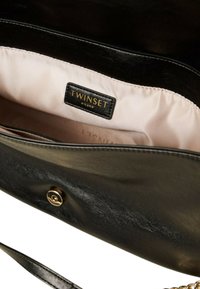 Čierna kožená kabelka s hladkou textúrou, s ružovou saténovou podšívkou a zlatou logovou nášivkou. Zapínanie na cvok.