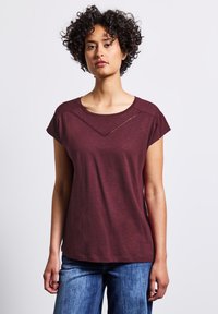 T-shirt bourgogne à manches courtes avec un col rond et un accent en découpe triangulaire juste en dessous des épaules, en tissu doux et léger.