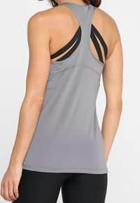 Grå atletisk linne med racerback-design och svarta remmar. Tillverkat av texturerad tyg, har det en figurnära silhuett och sömdetaljer.