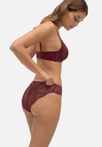 Conjunto de sujetador y braguitas de encaje burdeos, con patrones florales intrincados, textura suave, tirantes ajustables y bordes con forma de ondas.