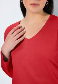 Rode V-hals lange mouwen shirt gemaakt van gladde katoenstof. Heeft een relaxte pasvorm, met een subtiele textuur en een eenvoudig ontwerp.