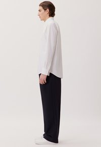 Witte lange mouwen overhemd met een getailleerde pasvorm, gecombineerd met ruime zwarte broeken en witte sneakers. Eenvoudig, strak ontwerp met minimale accenten.
