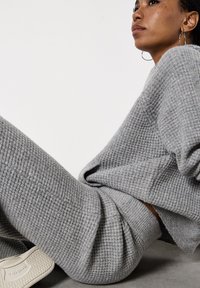 Maglione grigio a maglia con un motivo testurizzato a waffle, abbinato a pantaloni grigi a maglia coordinati. Sneakers bianche visibili in fondo.
