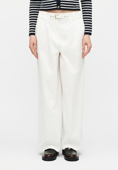 Femme portant un pantalon blanc taille haute à jambes larges avec détail ceinture, associé à un pull court rayé noir et blanc et des mocassins noirs.